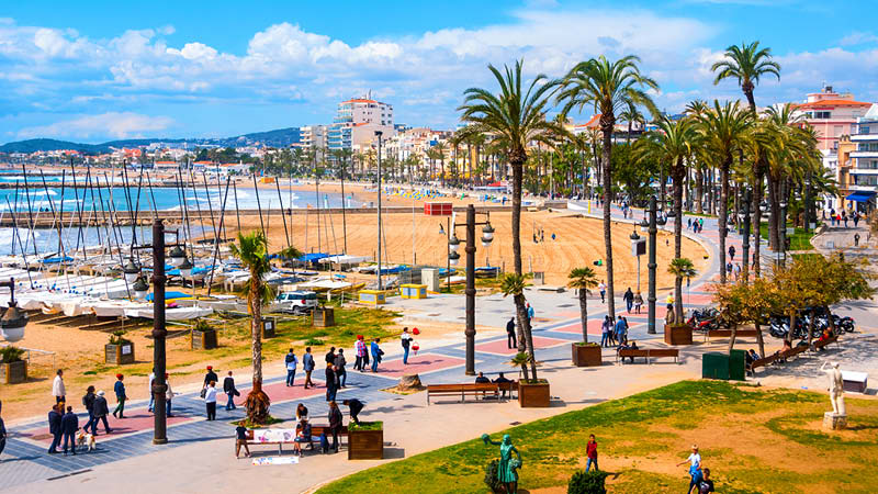 Den stora strandpromenaden med småbåtshamn, palmer och restauranger i Sitges, Spanien.